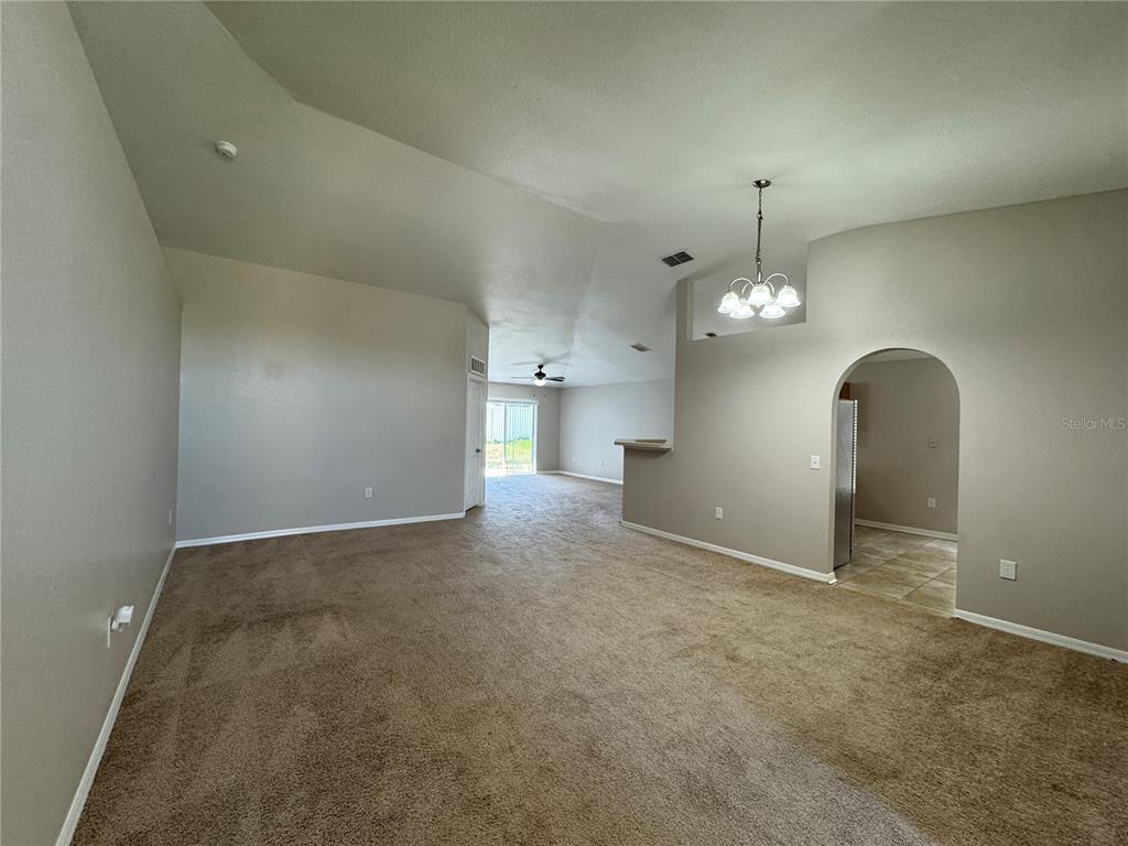 An empty living room with beige carpet, vaulted ceilings, and an arched entryway to the kitchen — 357 SQUIRES GROVE DRIVE, WINTER HAVEN, FL