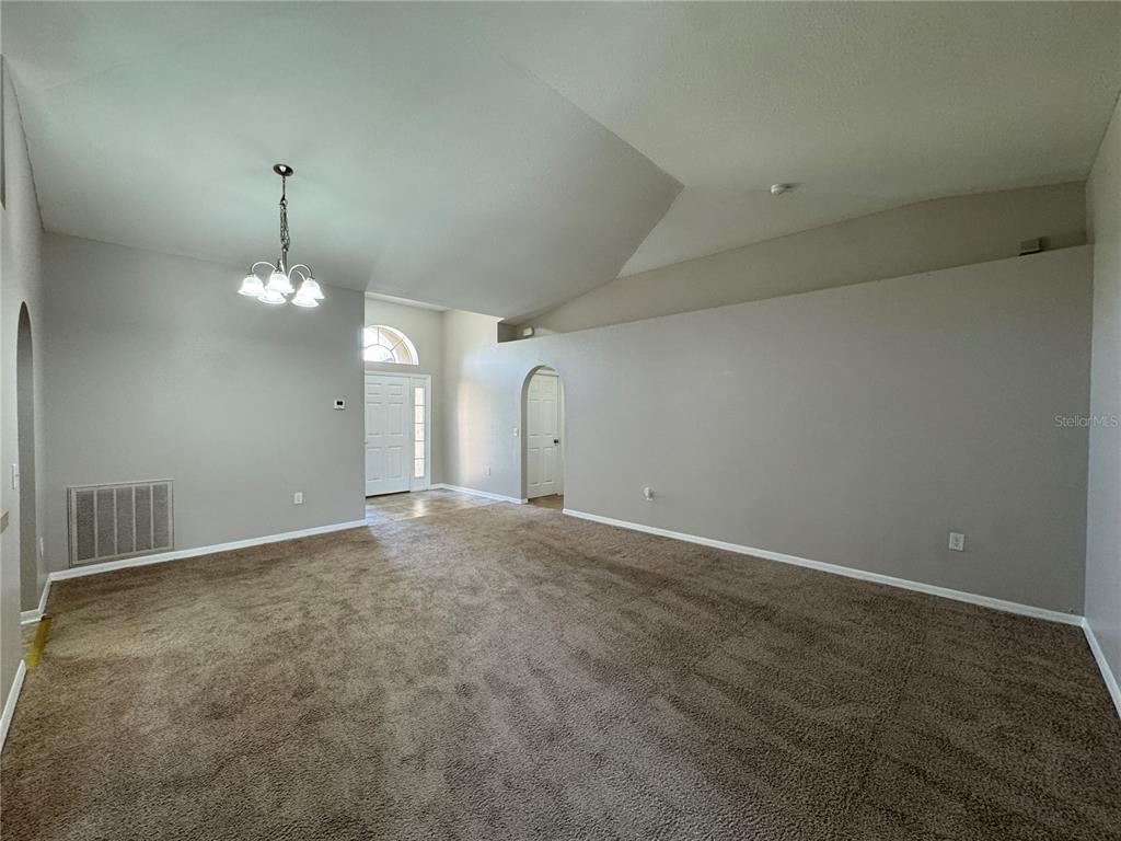A carpeted living room features a vaulted ceiling, a chandelier, and an arched doorway — 357 SQUIRES GROVE DRIVE, WINTER HAVEN, FL