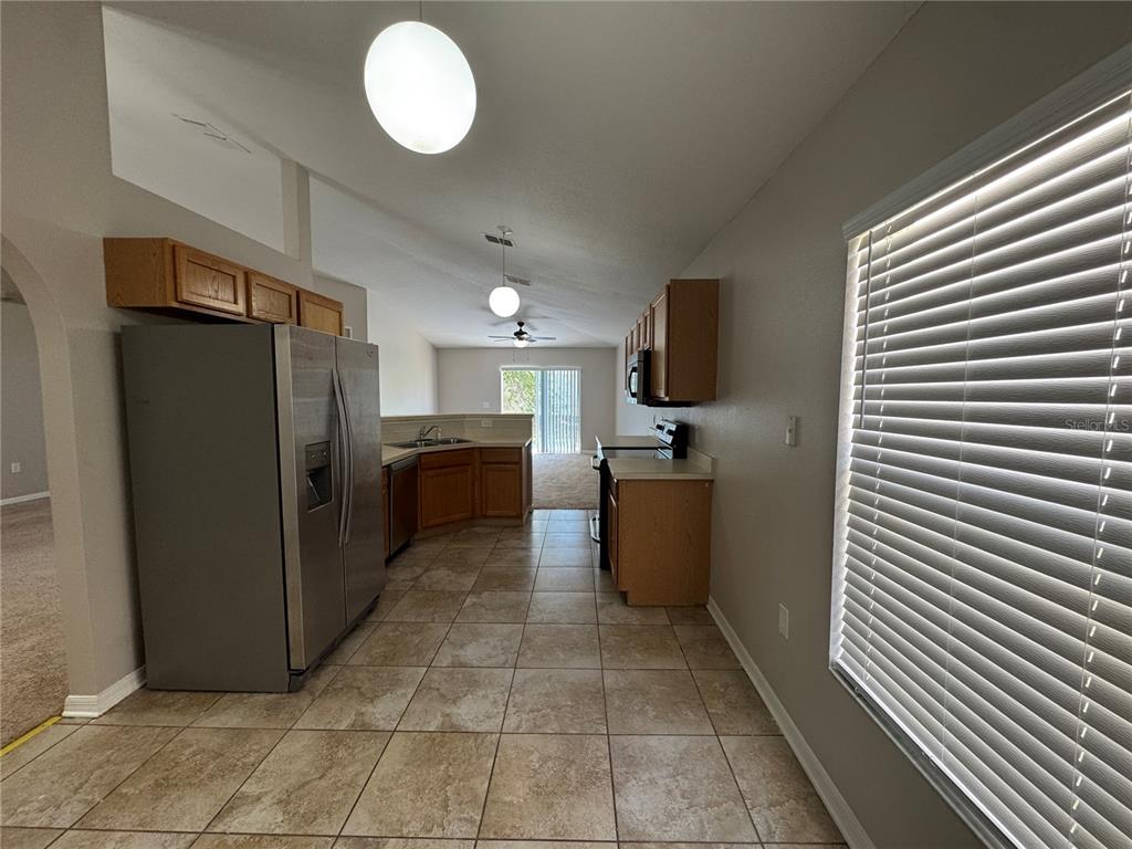 A kitchen with light-colored tile flooring, wood cabinets, stainless steel appliances, and vaulted ceilings — 357 SQUIRES GROVE DRIVE, WINTER HAVEN, FL