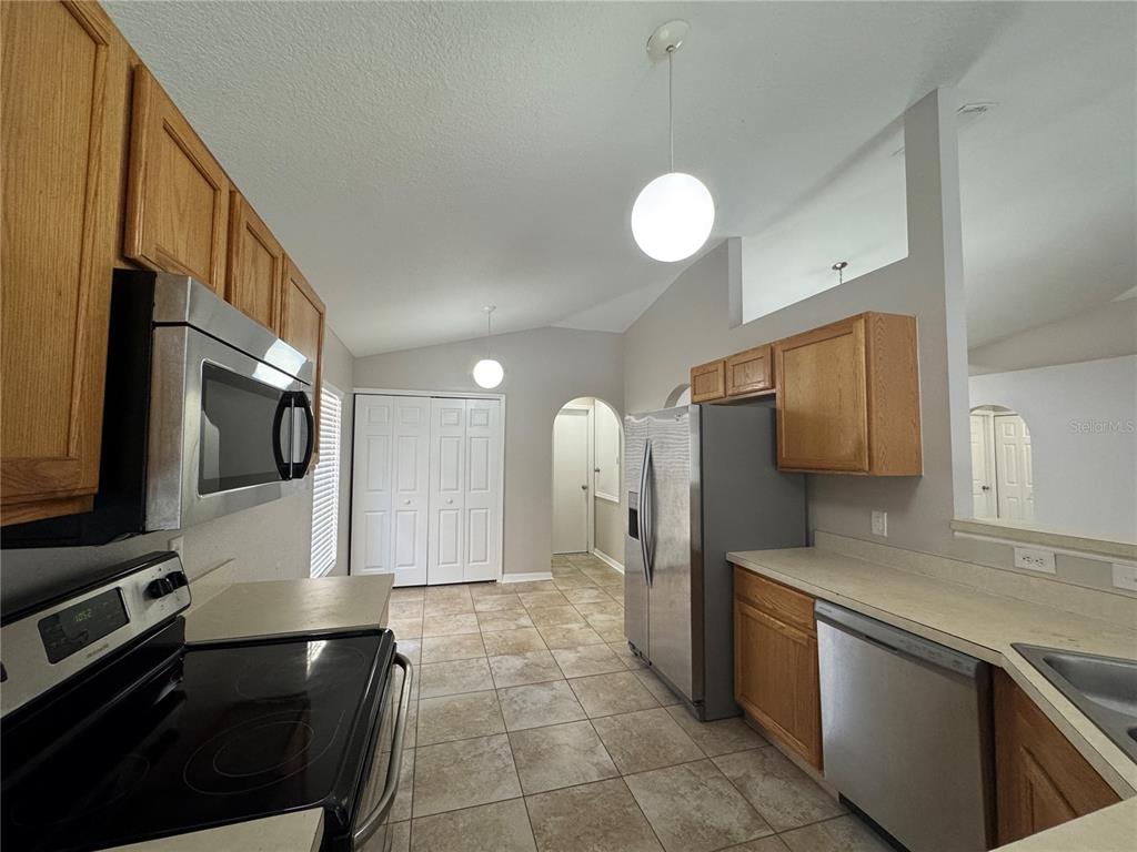 A kitchen features wood cabinets, stainless steel appliances, tile flooring, and two globe pendant lights — 357 SQUIRES GROVE DRIVE, WINTER HAVEN, FL