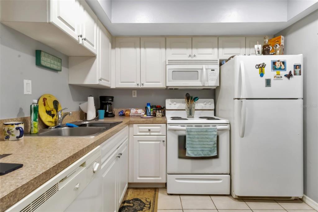 A kitchen features white cabinetry, white appliances, a double sink, and tan laminate countertops — 3100 HARBOR BOULEVARD UNIT 108, PORT CHARLOTTE, FL