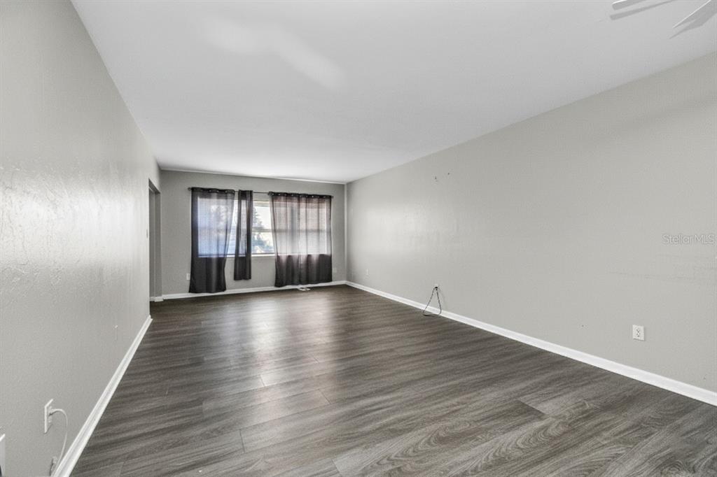 An empty living room features gray walls, dark wood-look flooring, and a window with curtains — 3100 HARBOR BOULEVARD UNIT 108, PORT CHARLOTTE, FL