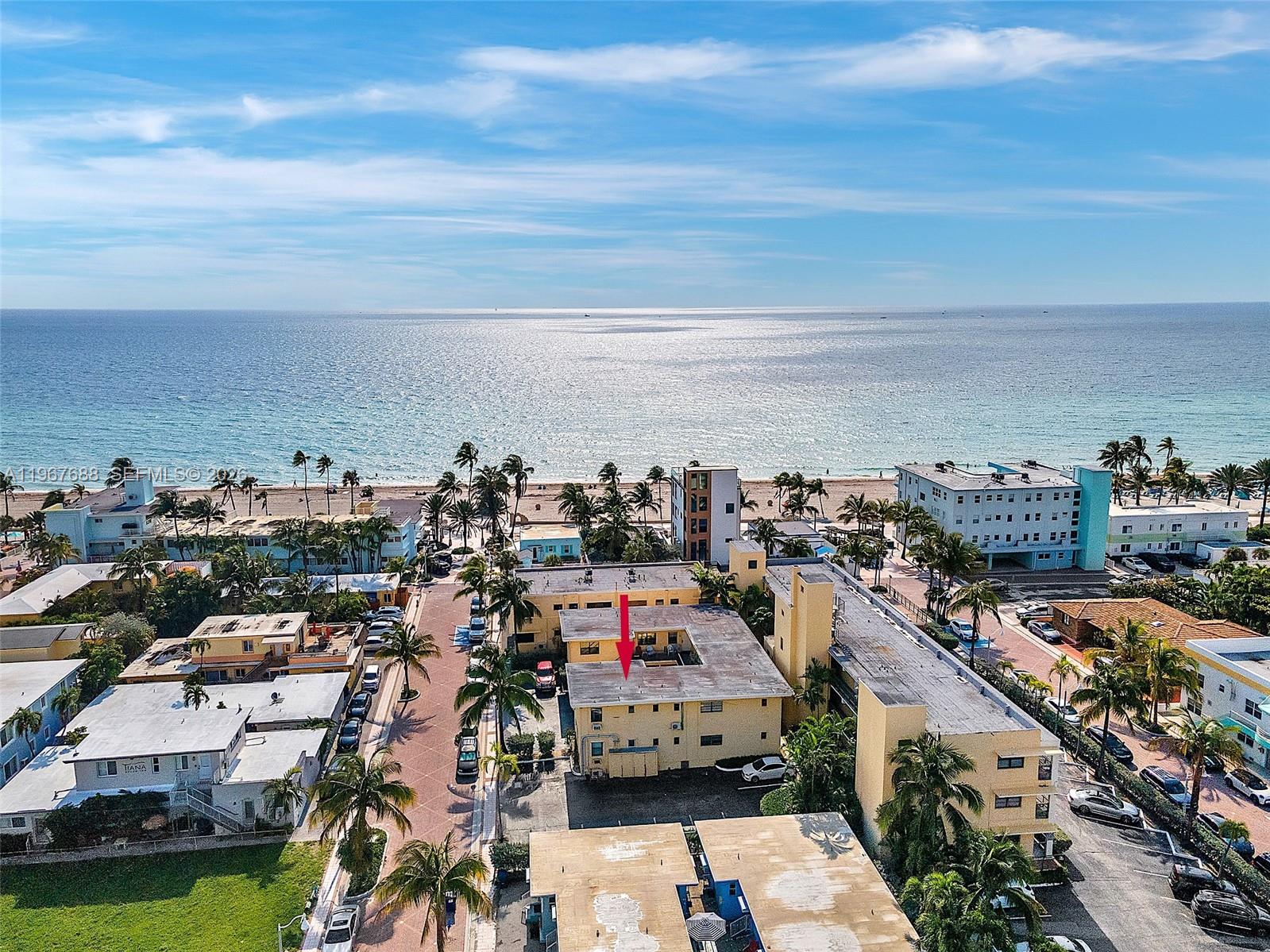 An aerial view shows a multi-story yellow apartment building near a sandy beach — 322 Harding St # B202, Hollywood FL 33019, HOLLYWOOD, FL