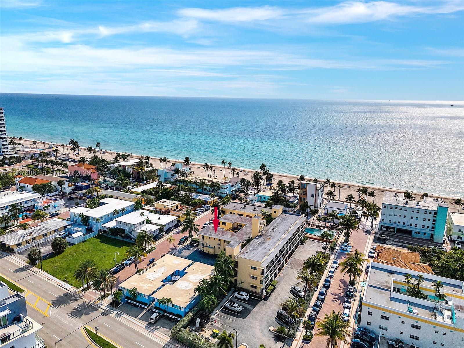 An aerial view shows a multi-story apartment building near a sandy beach and ocean — 322 Harding St # B202, Hollywood FL 33019, HOLLYWOOD, FL