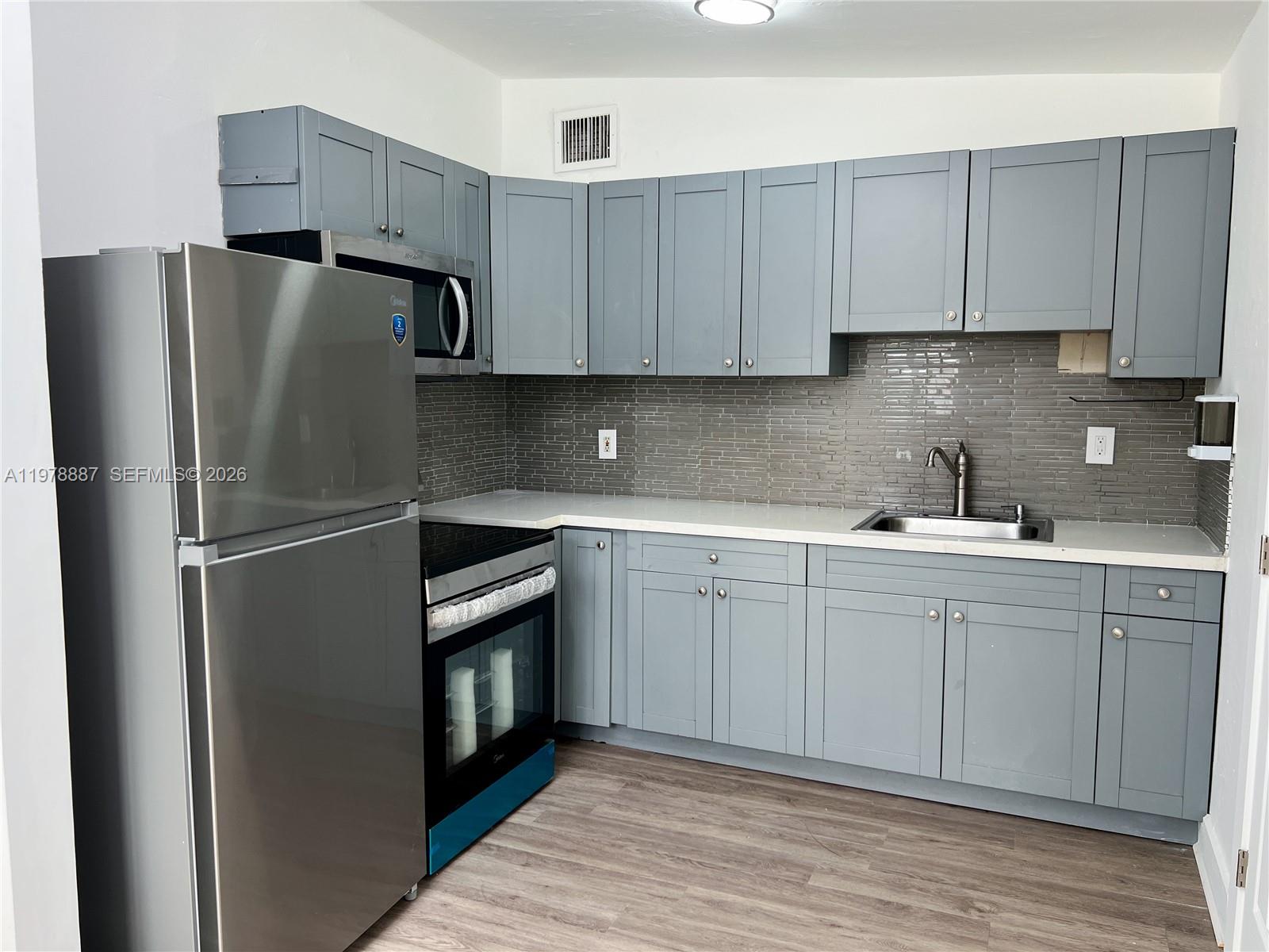A kitchen features gray shaker cabinets, stainless steel appliances, and a gray tiled backsplash — 10090 W Fern St, Miami FL 33157, MIAMI, FL