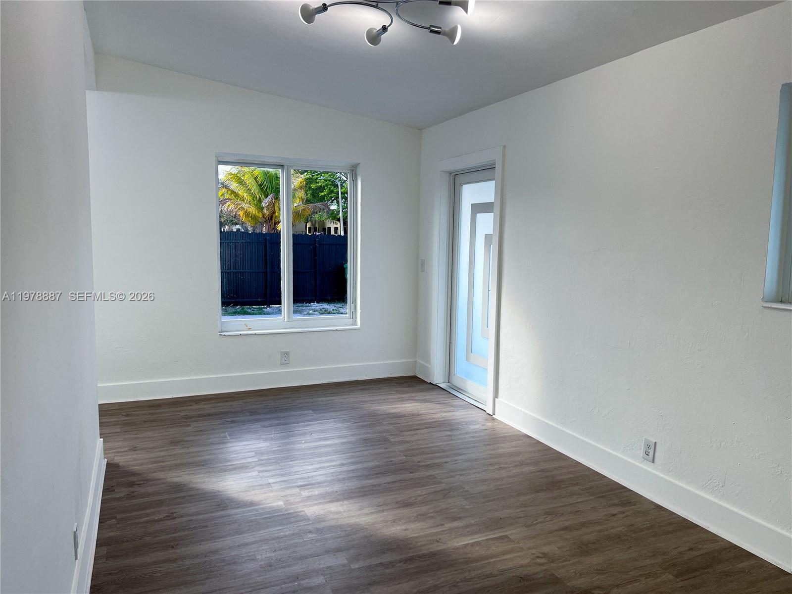 An empty room features white walls, wood-look flooring, a window, and a modern glass door — 10090 W Fern St, Miami FL 33157, MIAMI, FL