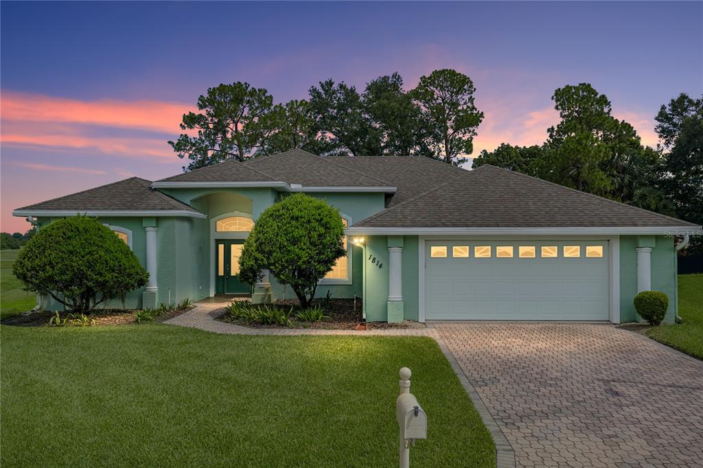 A single-story house with a light green exterior, a two-car garage, and a paved driveway — 1814 SANDHILL LANE, WINTER HAVEN, FL