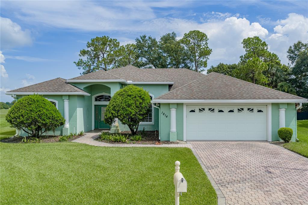 A single-story house with light green stucco walls, a shingled roof, and a paved driveway — 1814 SANDHILL LANE, WINTER HAVEN, FL