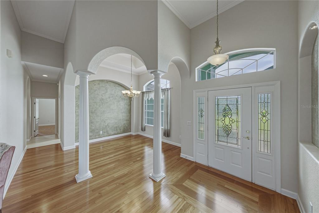 An entryway with hardwood floors, white columns, arched openings, and a glass-paneled front door — 1814 SANDHILL LANE, WINTER HAVEN, FL