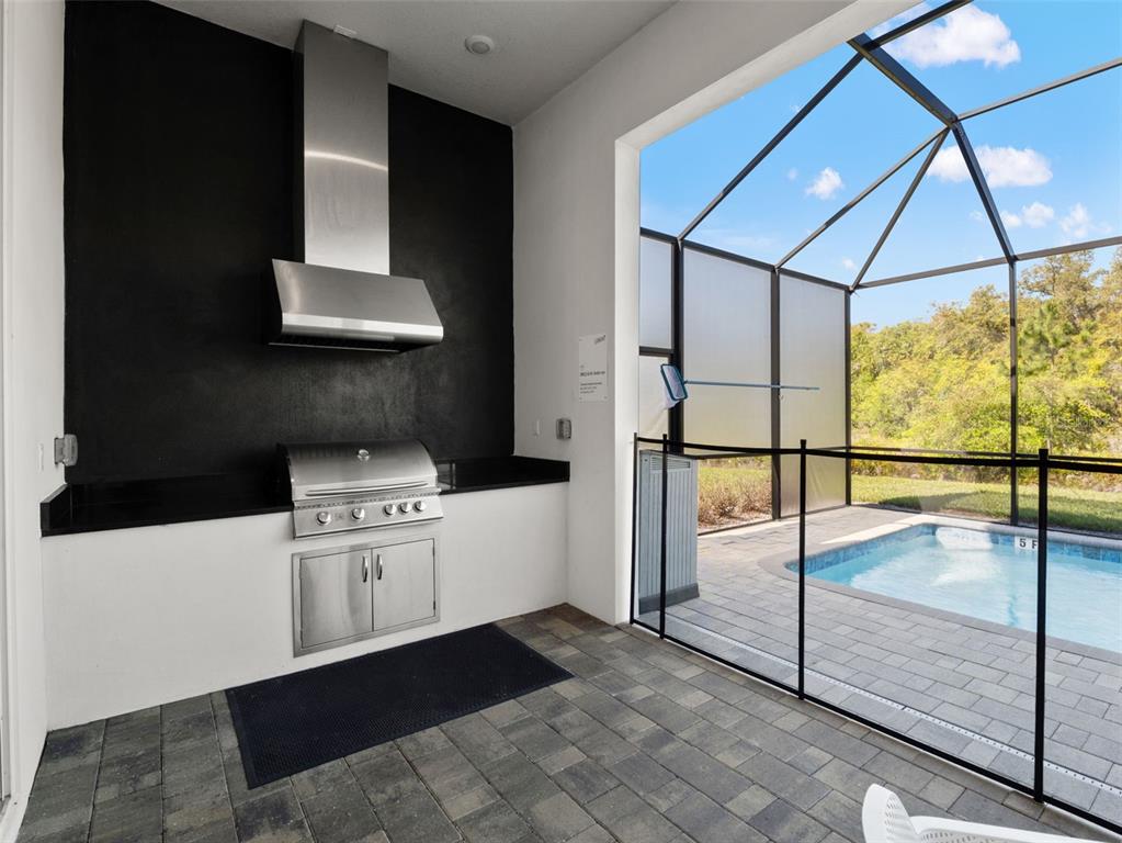 An outdoor kitchen with a stainless steel grill and hood overlooks a screened-in swimming pool — 2021 OAK CREEK LOOP, DAVENPORT, FL
