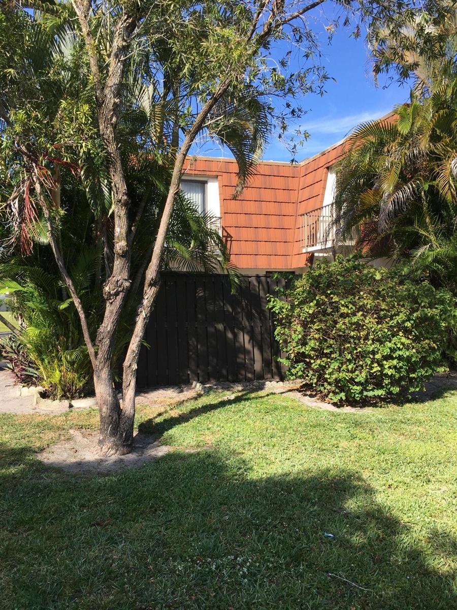 A two-story building with a brown tiled roof, a wooden fence, and surrounding tropical landscaping — 2233 White Pine Circle # D, FL 33415, FL