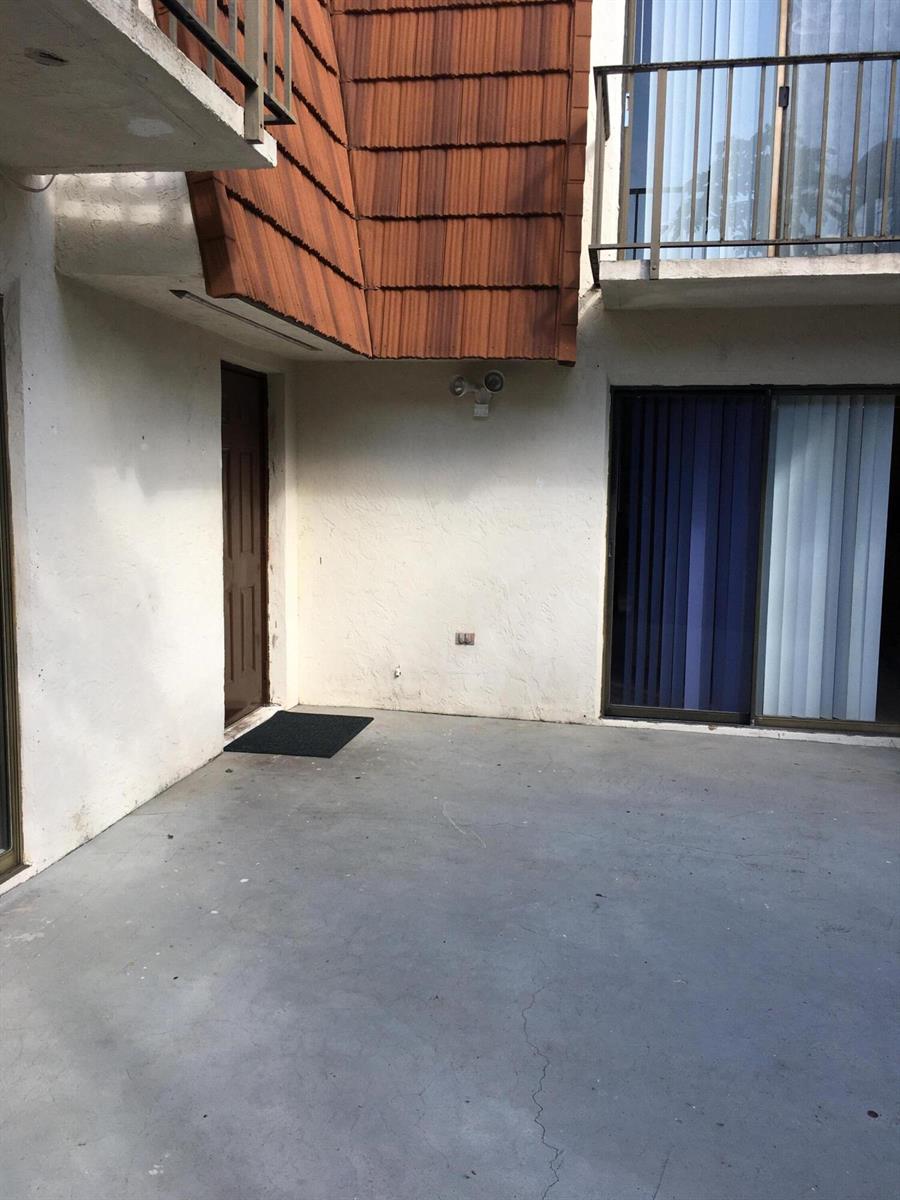 A concrete patio area features a brown door, sliding glass doors, and a shingled overhang — 2233 White Pine Circle # D, FL 33415, FL