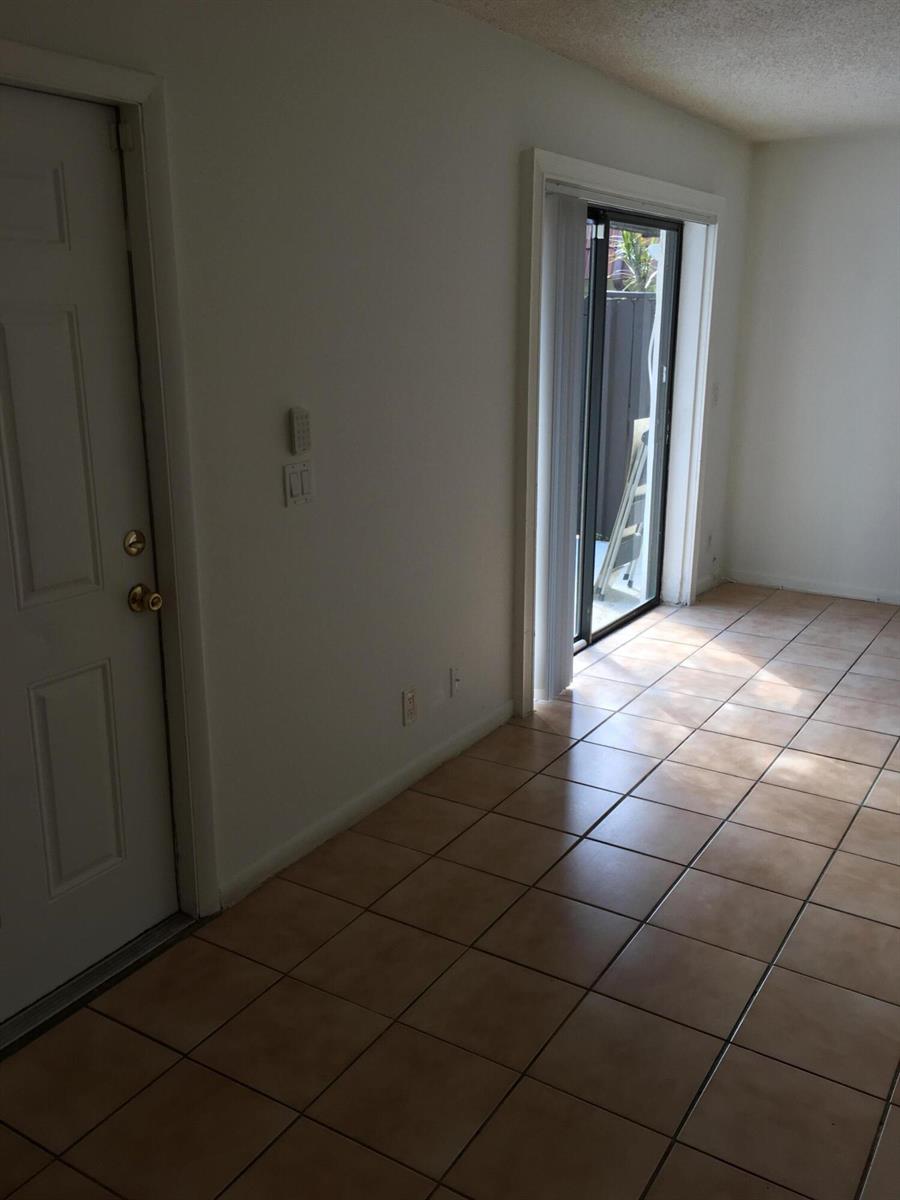 An interior view of a room with light-colored tile flooring, a white door, and sliding doors — 2233 White Pine Circle # D, FL 33415, FL