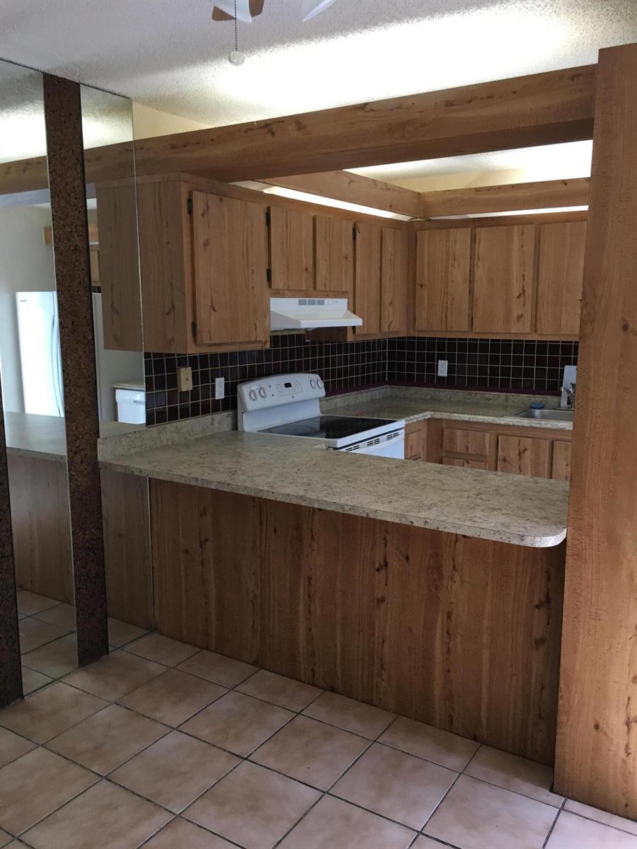 A kitchen features wood cabinets, a laminate countertop, a white stove, and dark tile backsplash — 2233 White Pine Circle # D, FL 33415, FL
