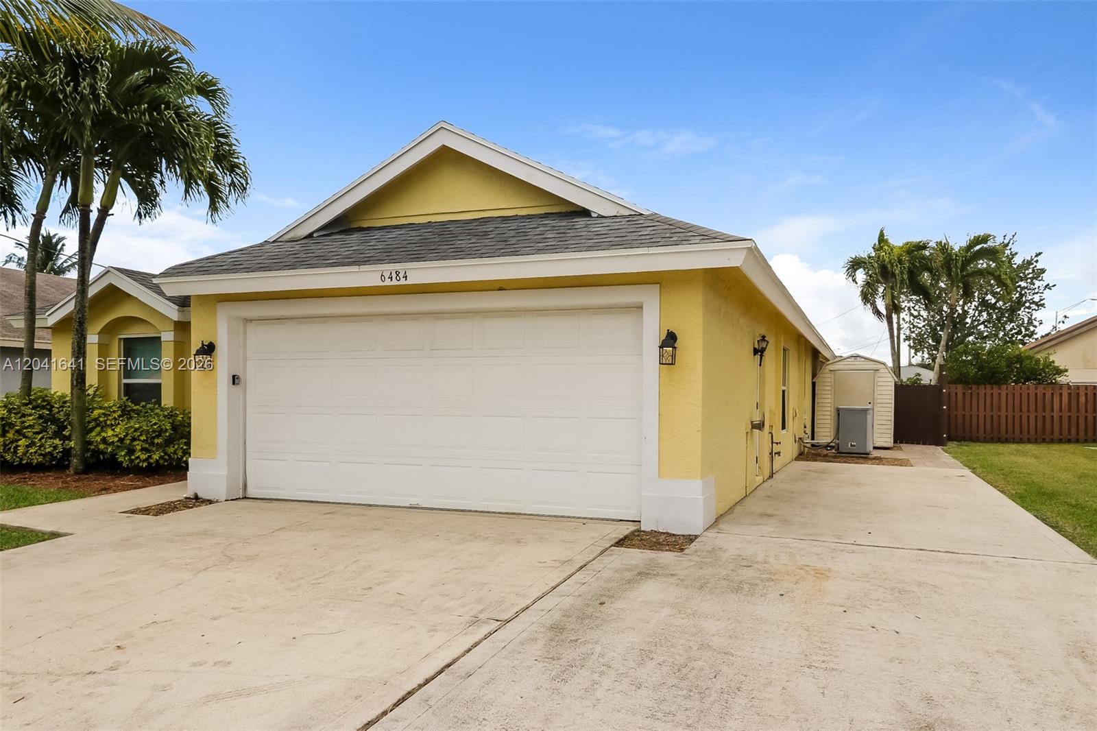 A yellow house exterior features a white garage door and a concrete driveway — 6484 Robinson St, Jupiter FL 33458, JUPITER, FL
