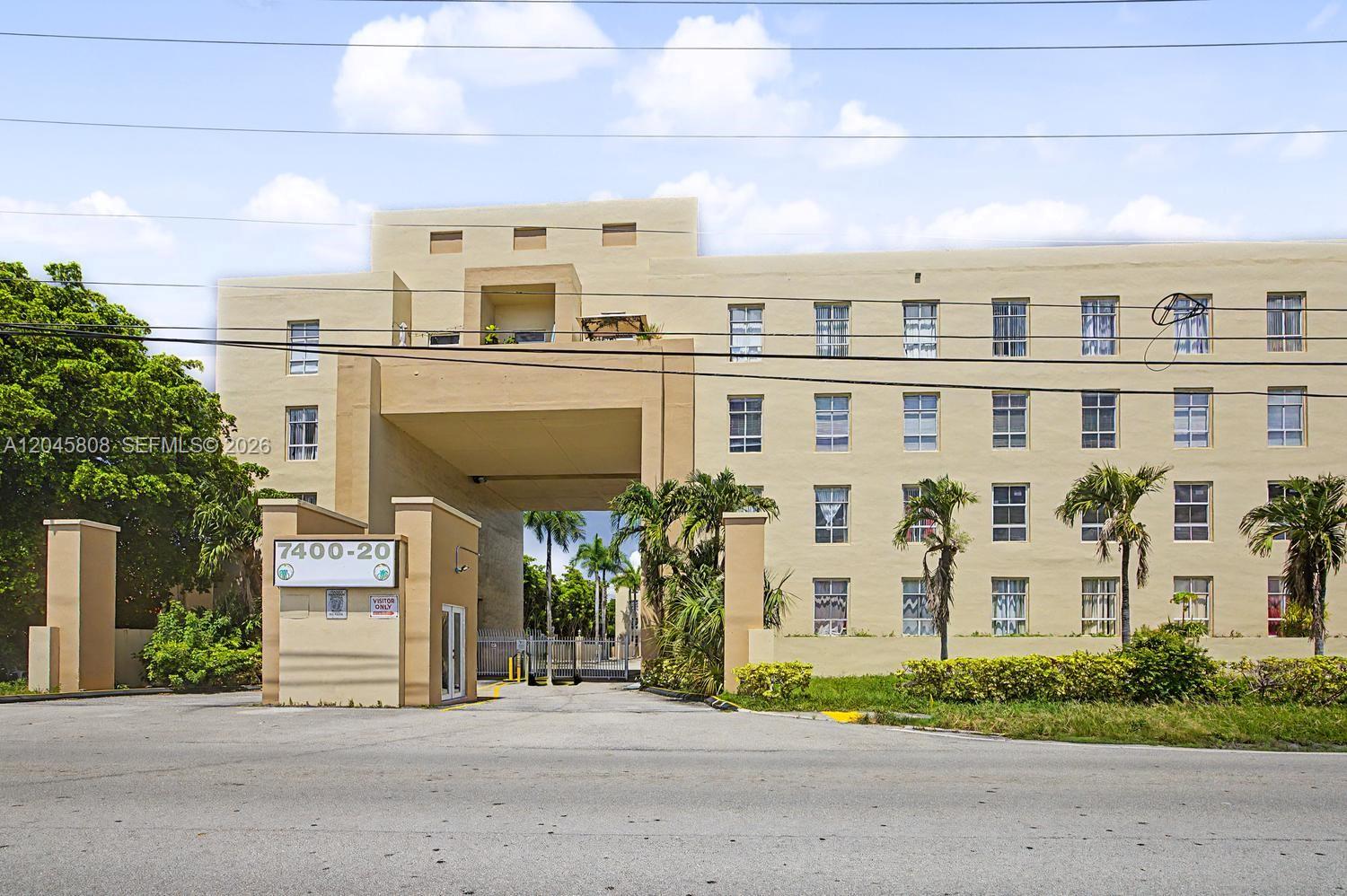 A multi-story beige apartment building features a large central archway entrance and palm trees — HIALEAH, FL
