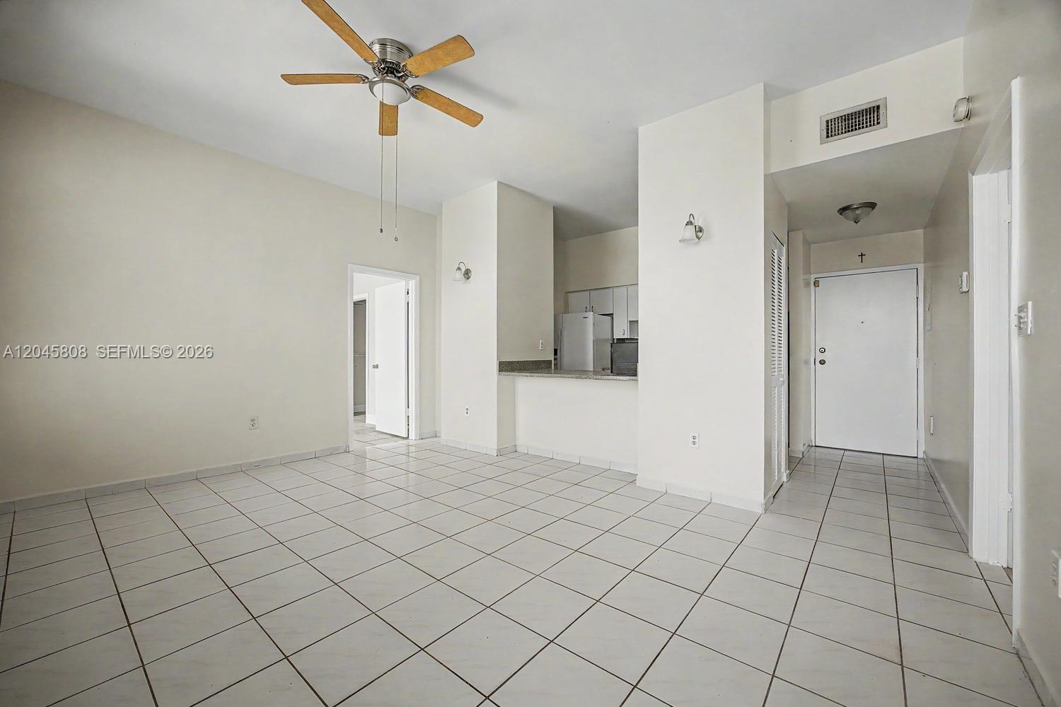 An open-concept living area features white tile flooring, a ceiling fan, and a kitchen pass-through — HIALEAH, FL