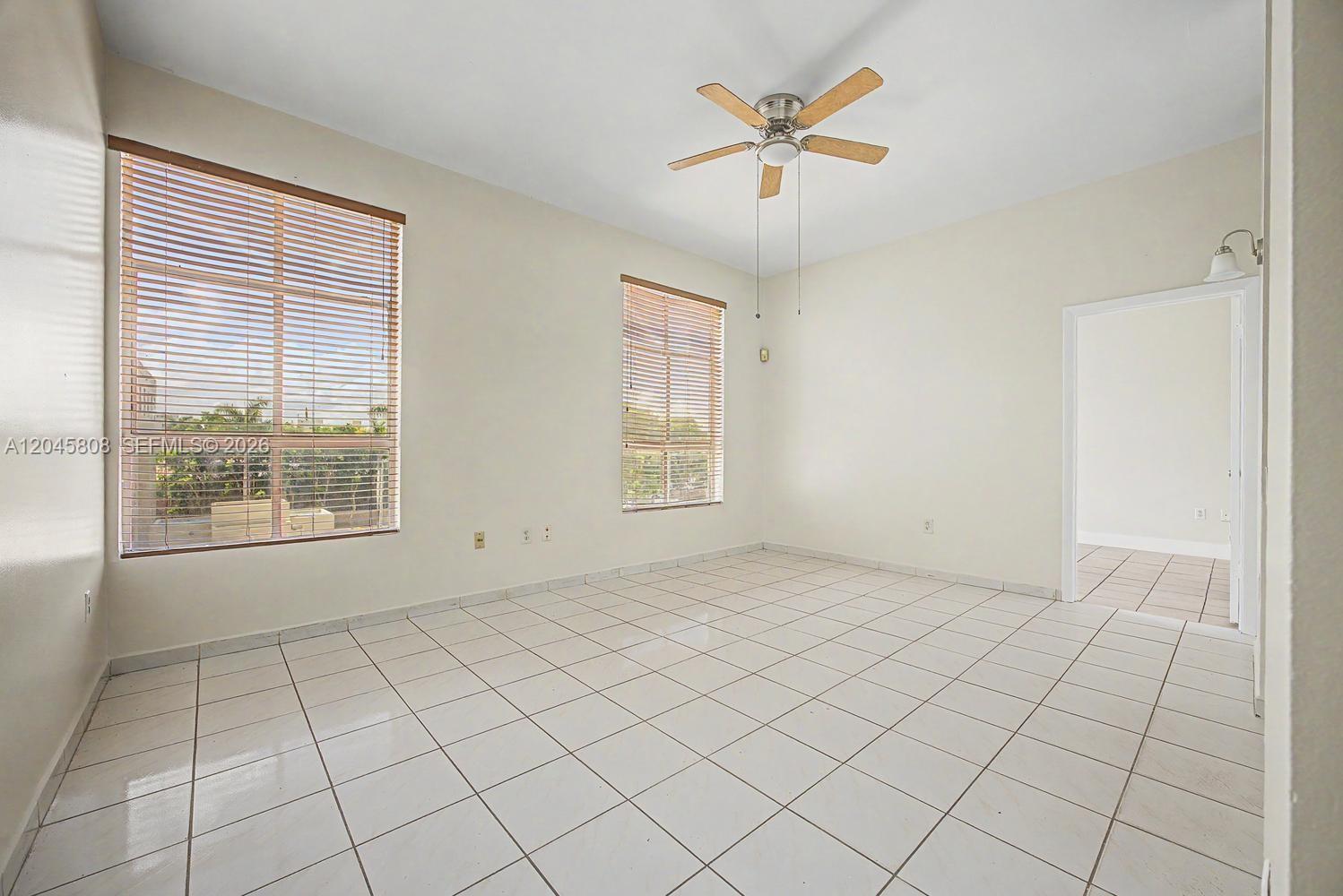 An empty room features white tile flooring, two windows with blinds, and a ceiling fan — HIALEAH, FL