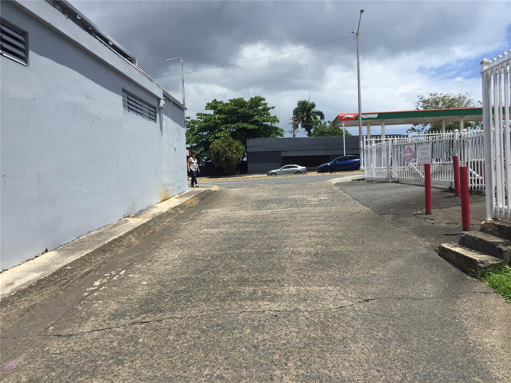 A paved driveway runs alongside a gray building toward a street and a gas station — 1710 Las Lomas Dev. JESUS T. PINERO AVE., SAN JUAN, PR