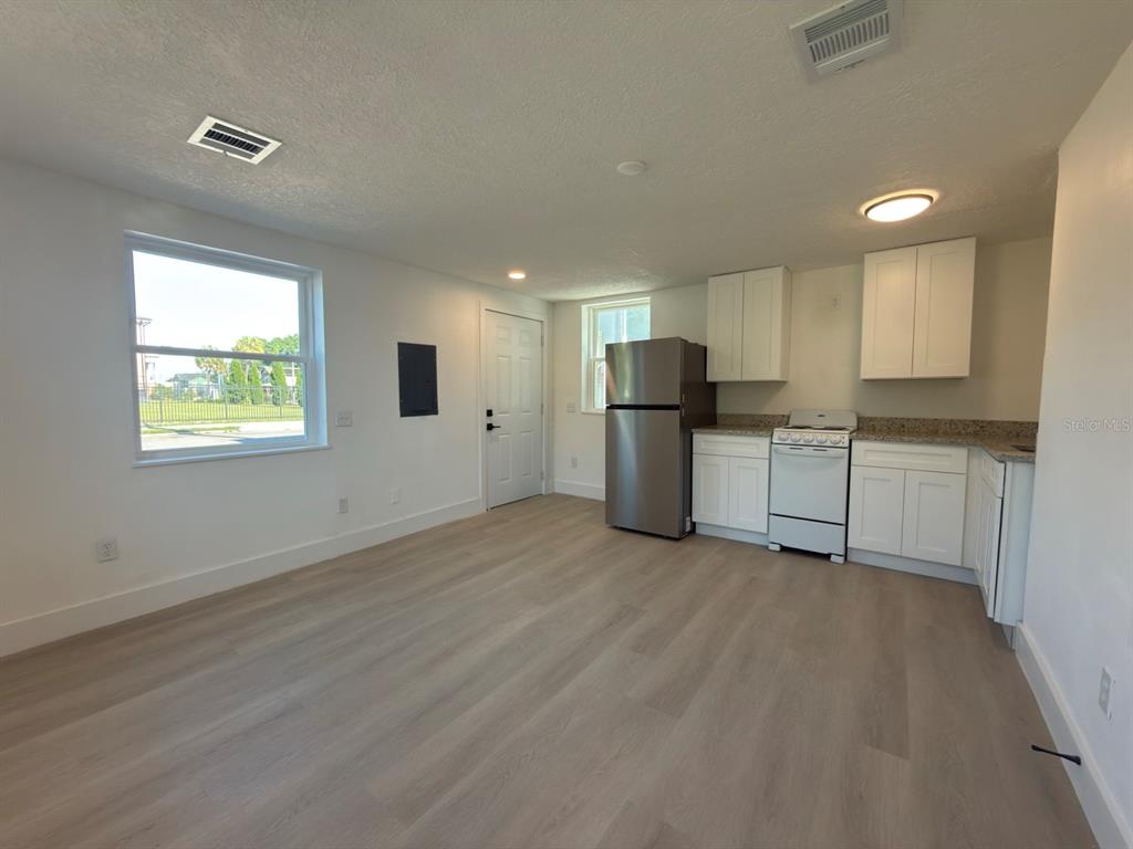 A kitchen and living area with white cabinets, stainless steel refrigerator, and light wood flooring — 401 E COLUMBUS DRIVE UNIT 2, TAMPA, FL