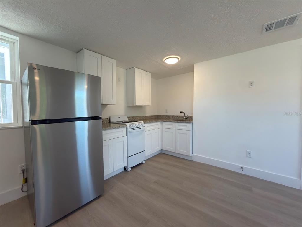 A kitchen features white cabinets, granite countertops, stainless steel appliances, and light wood-look flooring — 401 E COLUMBUS DRIVE UNIT 2, TAMPA, FL
