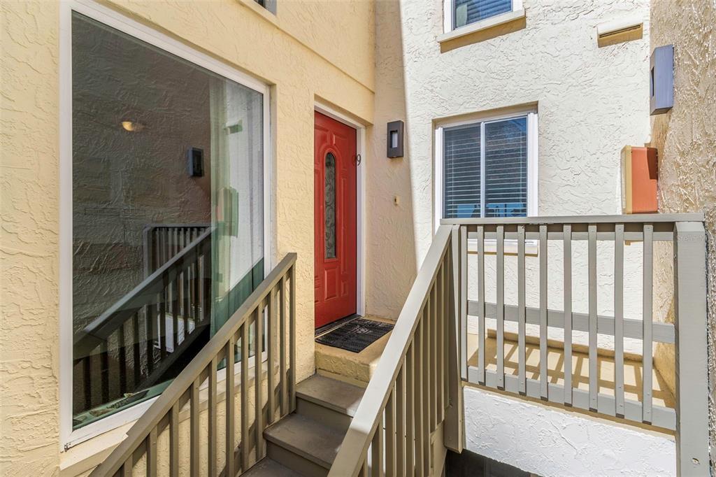 An exterior view of a building entrance with a red door and wooden stairs — 20204 GULF BOULEVARD UNIT 9, INDIAN SHORES, FL