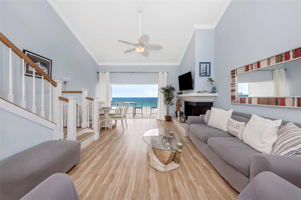 A living room features light wood floors, a gray sofa, and a balcony overlooking the ocean — 20204 GULF BOULEVARD UNIT 9, INDIAN SHORES, FL