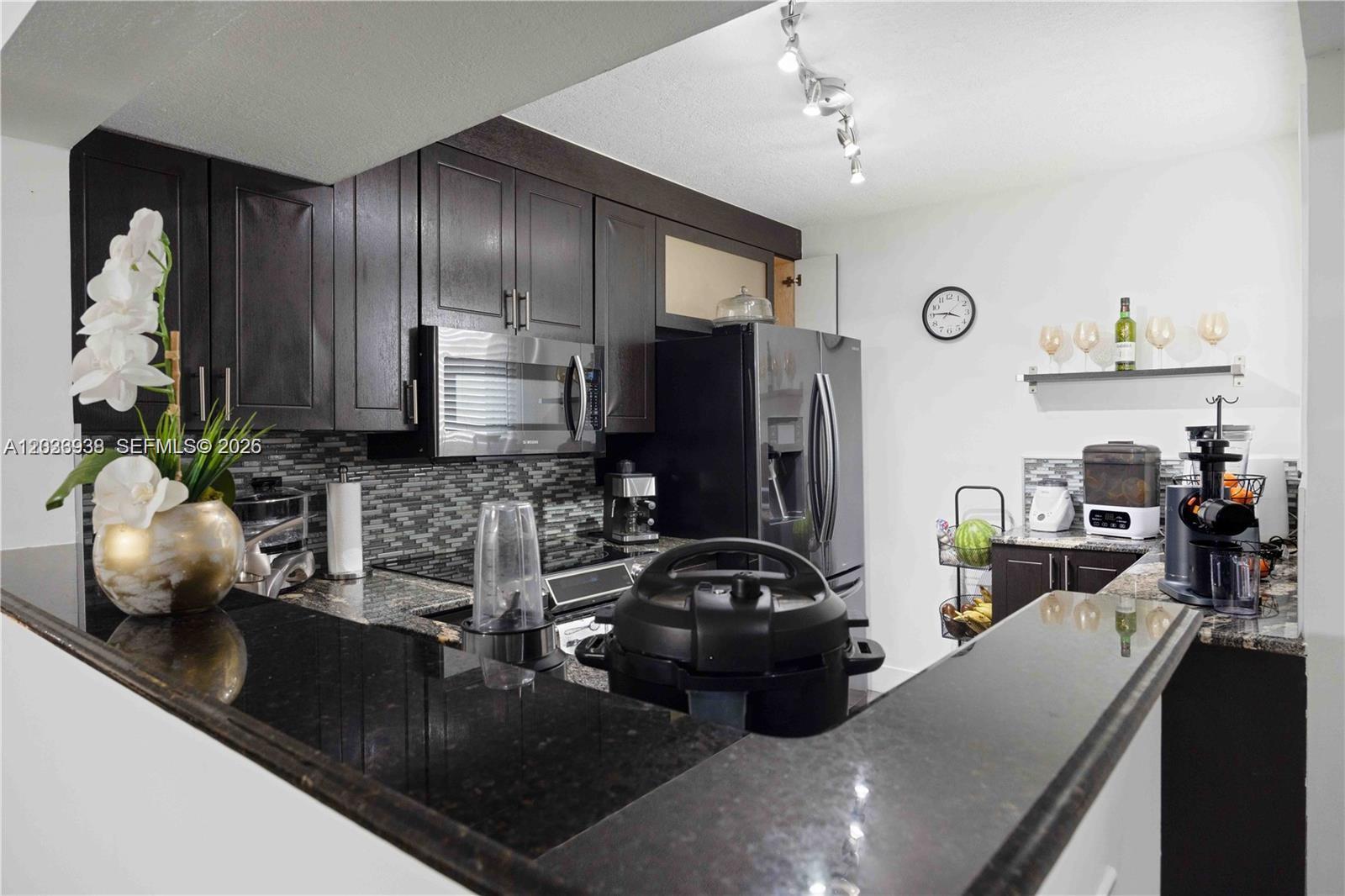 A kitchen features dark wood cabinets, black granite countertops, stainless steel appliances, and a backsplash — 12505 NW 11th Ln # 109, Miami FL 33182, MIAMI, FL