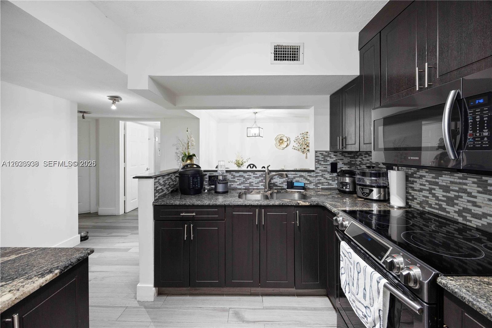 A kitchen features dark wood cabinets, granite countertops, and a tiled backsplash — 12505 NW 11th Ln # 109, Miami FL 33182, MIAMI, FL