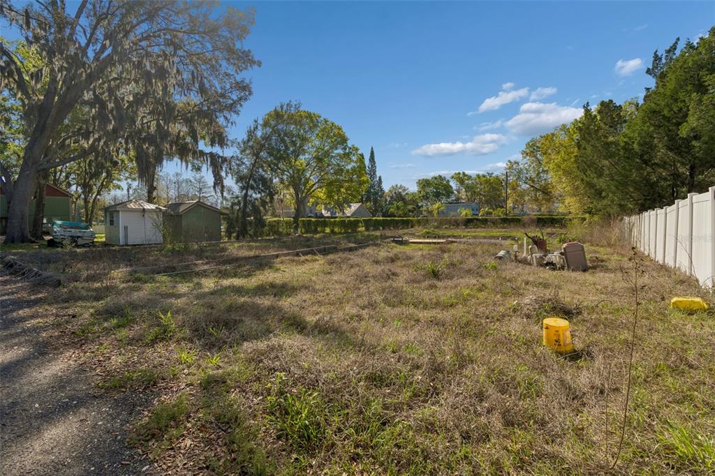An overgrown, vacant lot features two small sheds, a white fence, and mature trees — 8715 BROOKE ANGELA DRIVE, ODESSA, FL