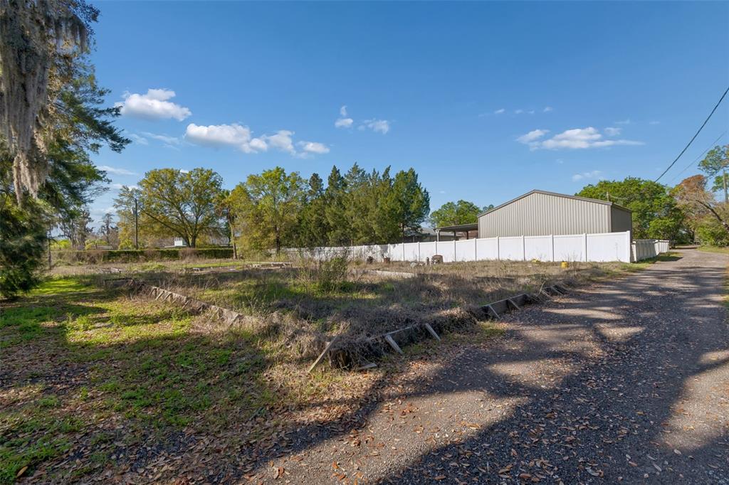 A gravel path runs alongside a vacant, overgrown lot bordered by a white vinyl fence — 8715 BROOKE ANGELA DRIVE, ODESSA, FL