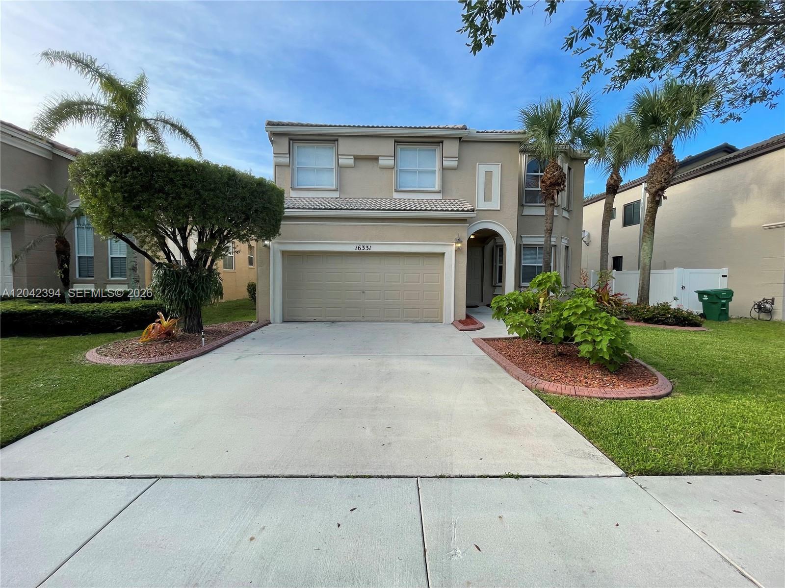 A two-story beige house features a two-car garage, palm trees, and a concrete driveway — MIRAMAR, FL