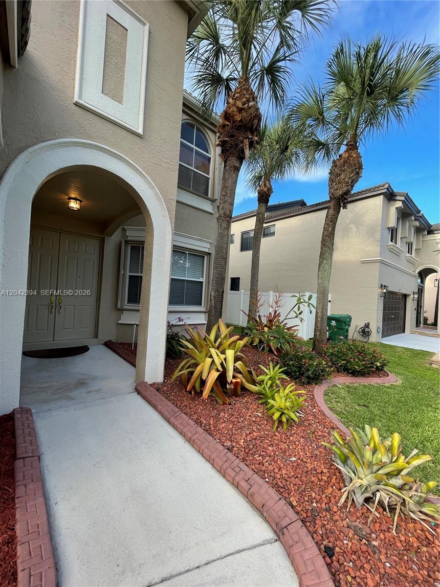 A concrete walkway leads to the arched entryway of a two-story house with palm trees — MIRAMAR, FL