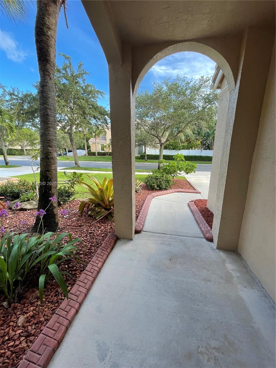 A covered entryway leads to a concrete walkway surrounded by landscaping and red mulch — MIRAMAR, FL