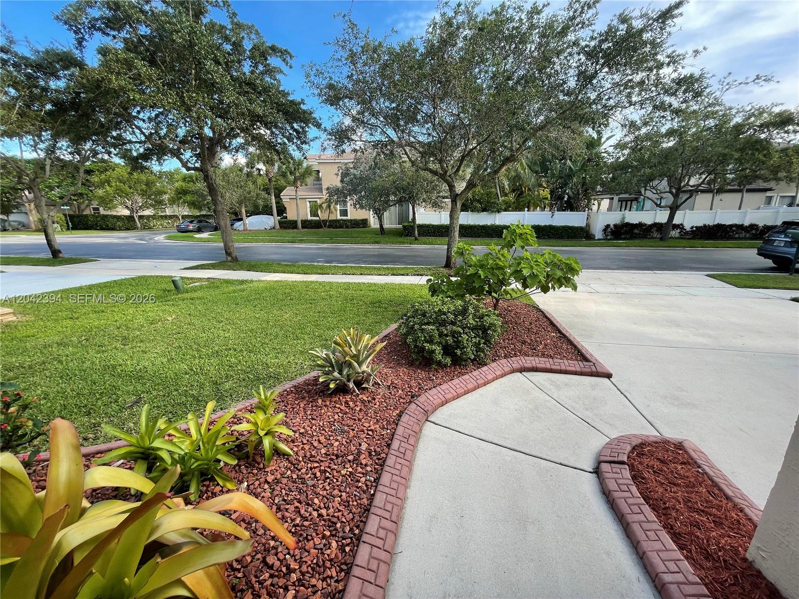 A landscaped front yard features red gravel mulch, brick edging, and a concrete walkway — MIRAMAR, FL
