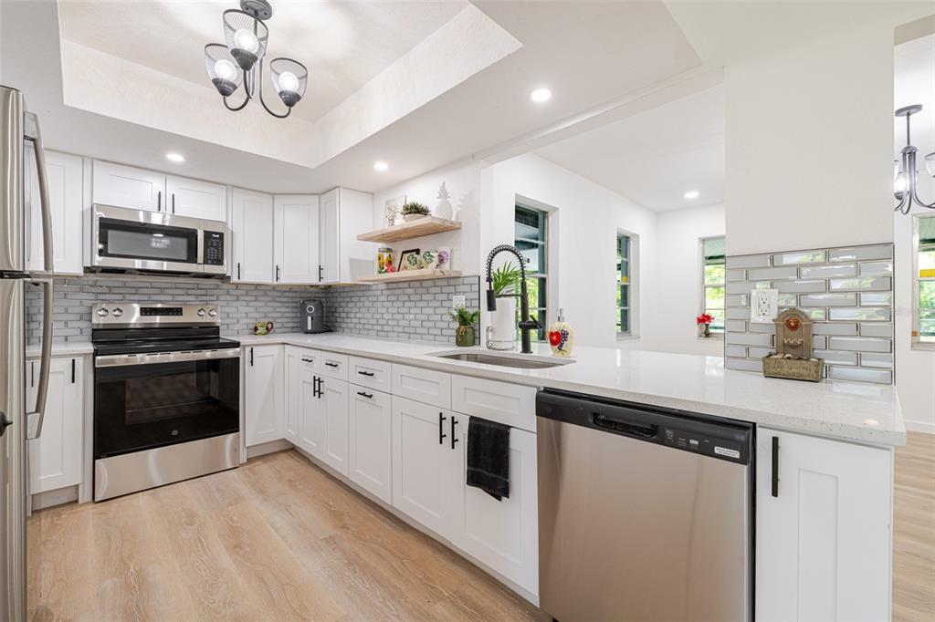 A modern kitchen features white cabinets, stainless steel appliances, quartz countertops, and gray subway tile — 4211 5TH STREET W, LEHIGH ACRES, FL