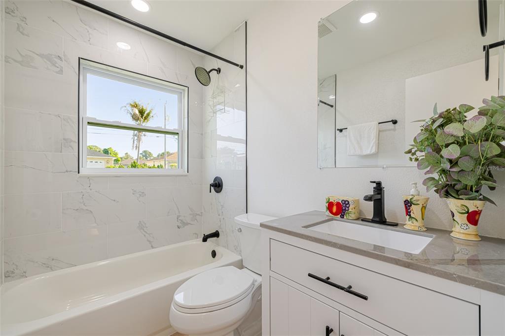 A bathroom features a white vanity, a toilet, and a bathtub with marble-look tile walls — 4211 5TH STREET W, LEHIGH ACRES, FL