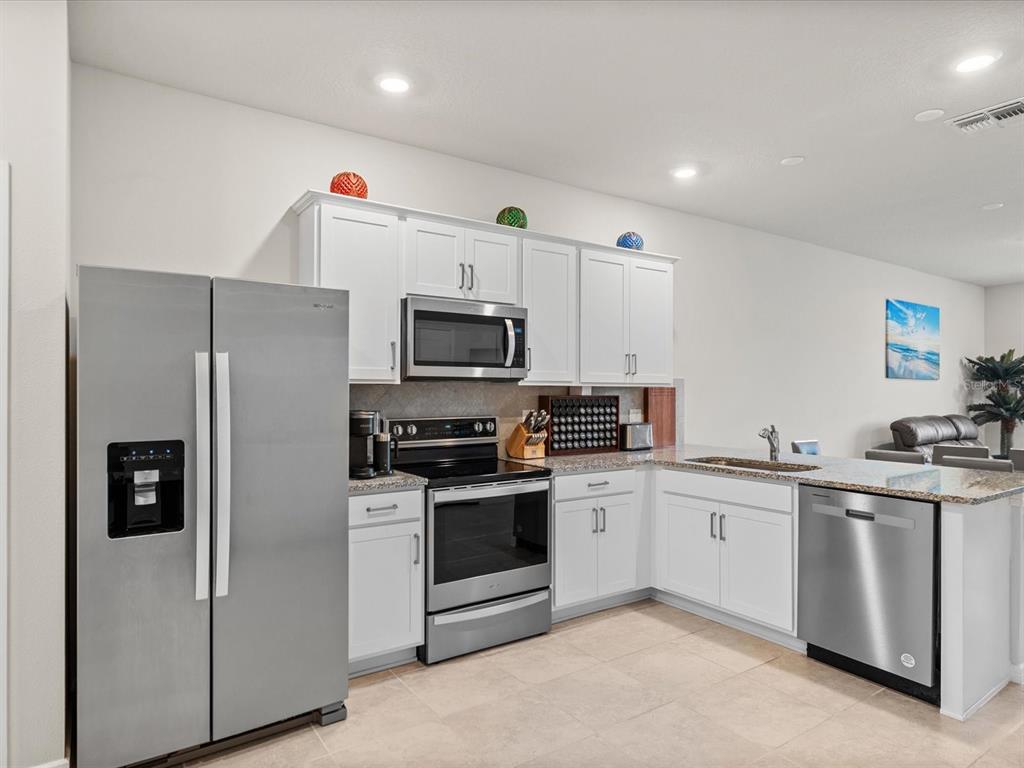 A kitchen features white cabinets, stainless steel appliances, and granite countertops with a tile backsplash — 31428 AMBERVIEW BEND, WESLEY CHAPEL, FL