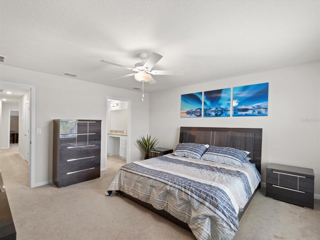 A bedroom features a bed with striped bedding, dark wood furniture, and wall art — 31428 AMBERVIEW BEND, WESLEY CHAPEL, FL