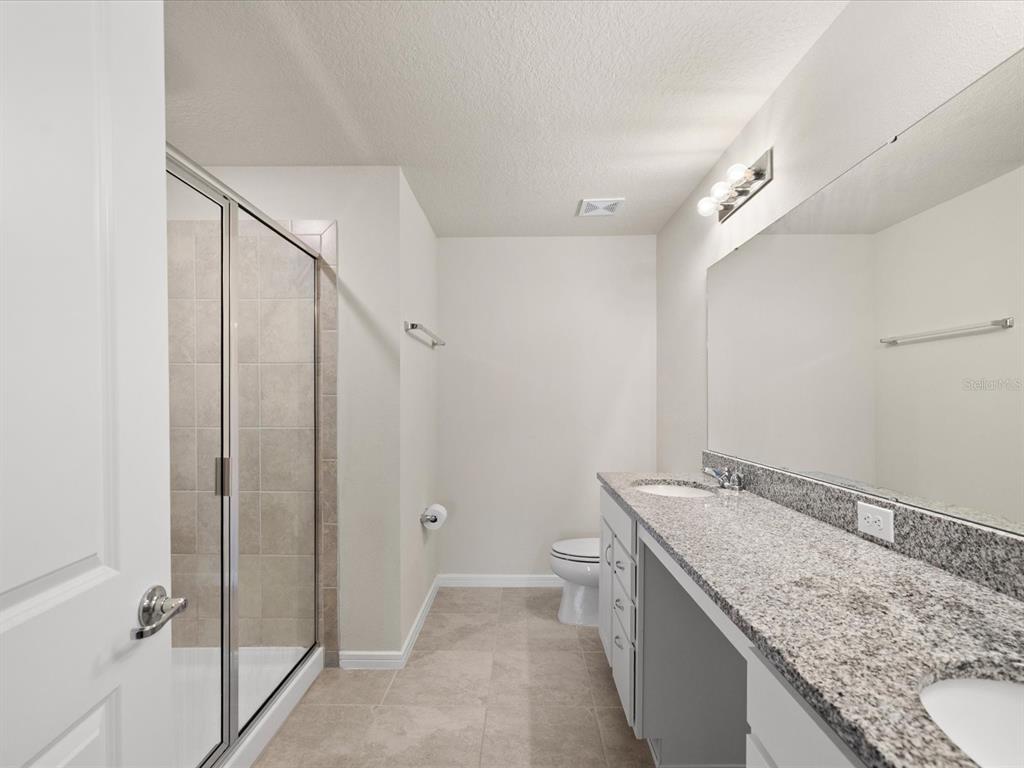 A bathroom features a glass-enclosed shower, a double vanity with granite countertops, and tile flooring — 31428 AMBERVIEW BEND, WESLEY CHAPEL, FL