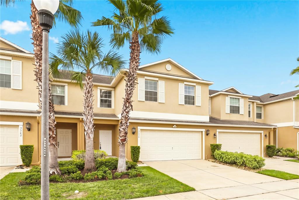 A two-story tan townhouse features a two-car garage, palm trees, and a landscaped front yard — 3538 RODRICK CIRCLE, ORLANDO, FL