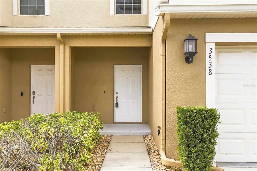 The exterior of a tan townhouse features a white front door, a walkway, and landscaping — 3538 RODRICK CIRCLE, ORLANDO, FL