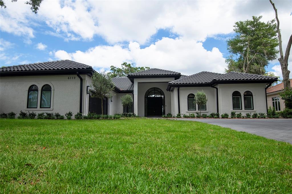 A single-story house with a dark tiled roof, white stucco walls, and a paved driveway — 6119 PAYNE STEWART DRIVE, WINDERMERE, FL