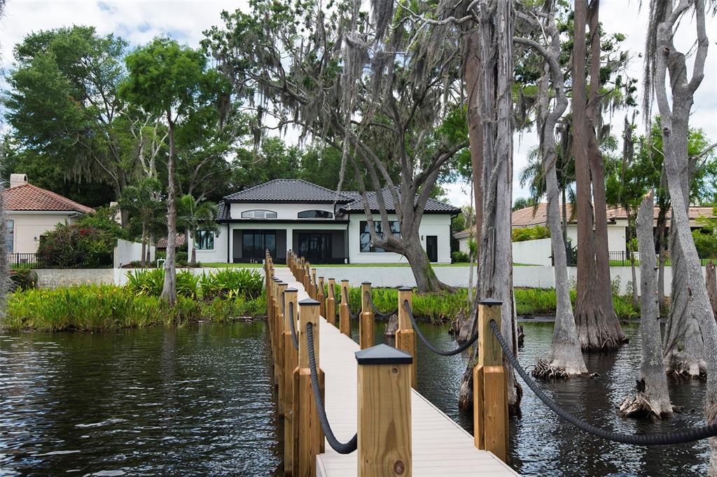 A wooden dock with rope railings leads toward a white house surrounded by cypress trees — 6119 PAYNE STEWART DRIVE, WINDERMERE, FL