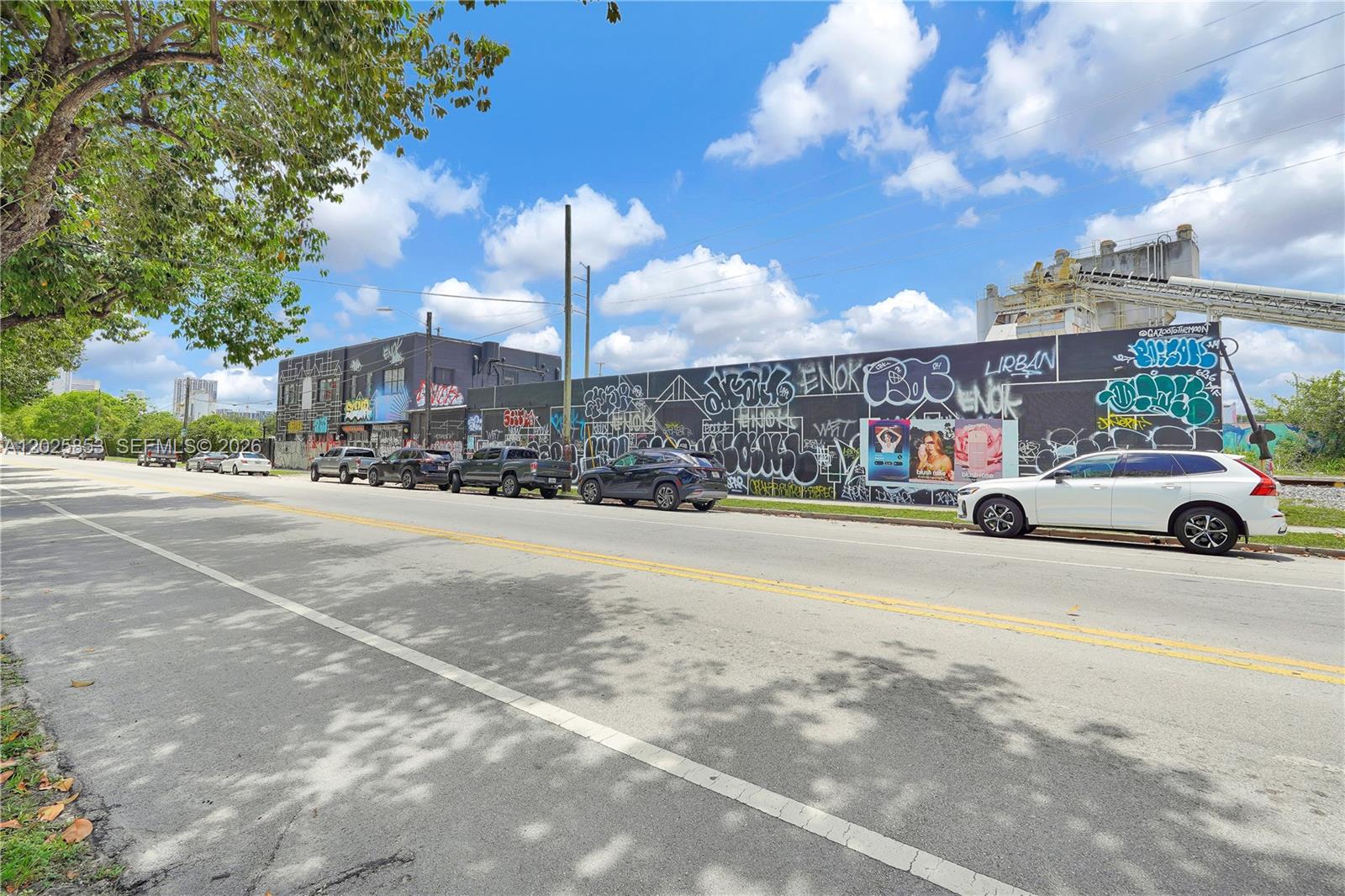 A street view shows a long, graffiti-covered wall next to parked cars under a blue sky — MIAMI, FL