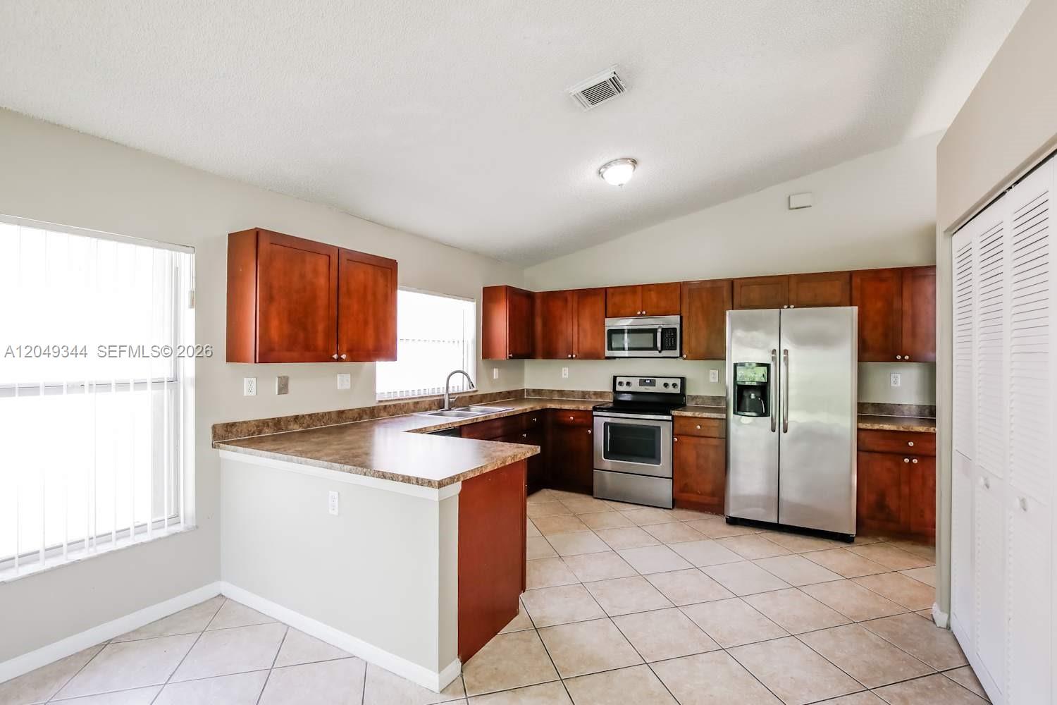 A kitchen features wood cabinets, stainless steel appliances, and a peninsula counter on tile flooring — PEMBROKE PINES, FL
