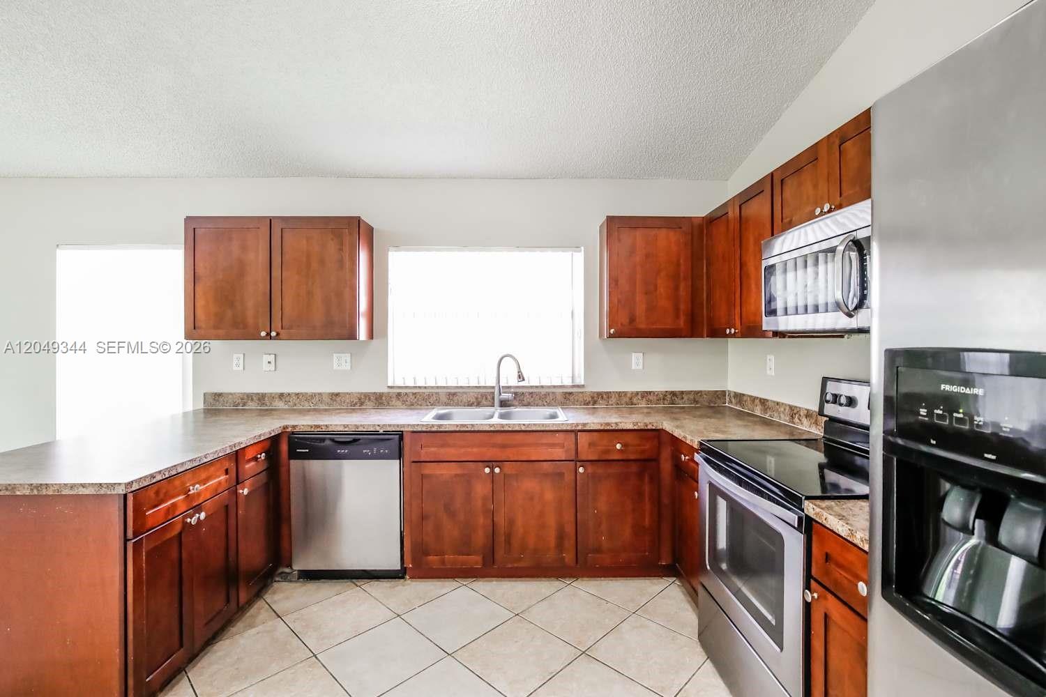 A kitchen features cherry wood cabinets, stainless steel appliances, and beige tile flooring — PEMBROKE PINES, FL
