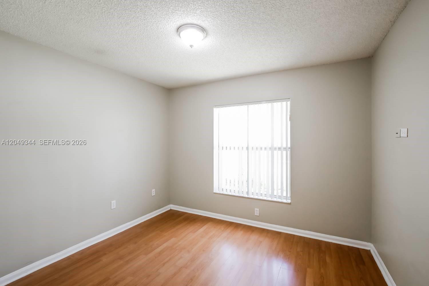 An empty bedroom features light gray walls, wood-look flooring, and a window with vertical blinds — PEMBROKE PINES, FL