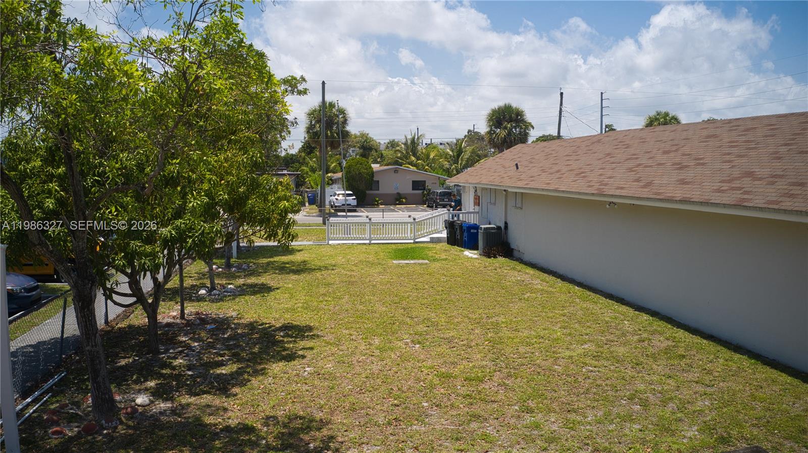 A grassy backyard area sits beside a house with a brown shingled roof — 15947 NE 19th Pl, North Miami Beach FL 33162, NORTH MIAMI BEACH, FL