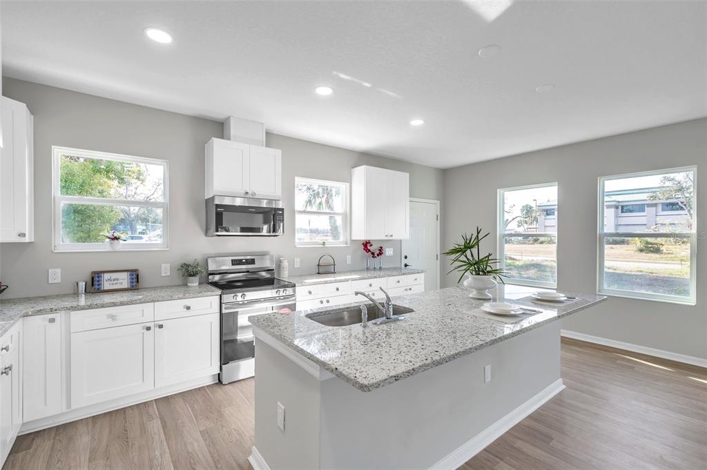 A kitchen features white cabinets, granite countertops, a center island, and light wood-look flooring — 5742 MEADOWLANE STREET, NEW PORT RICHEY, FL